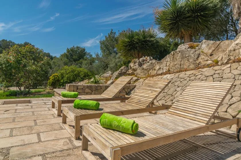 Wooden lounge chairs with green cushions sit beside a stone terrace wall.