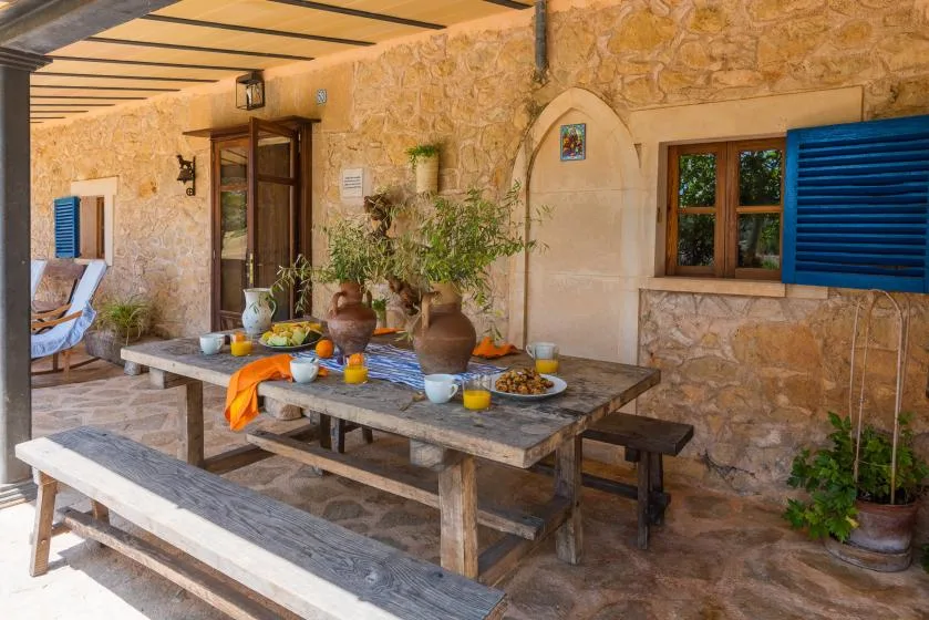 A covered stone patio with a dining table set with dishes and potted plants.