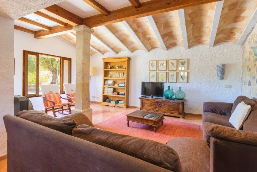 A living room with seating, a television, and exposed wooden ceiling beams.