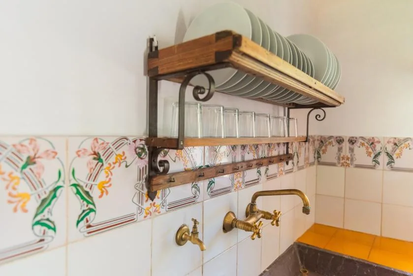 A kitchen sink area with a wall-mounted dish rack and patterned tile.