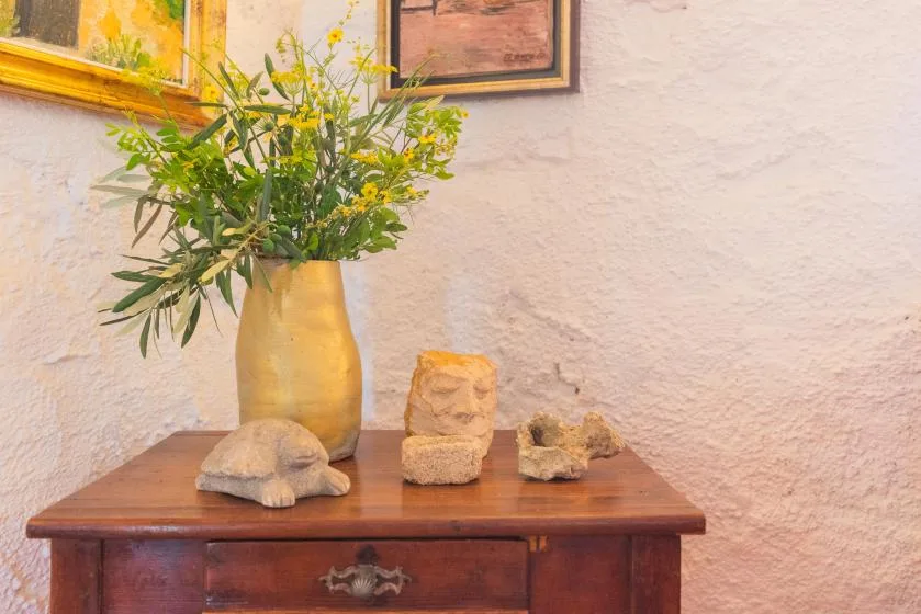 A wooden table displays a vase of yellow flowers and small decorative objects.