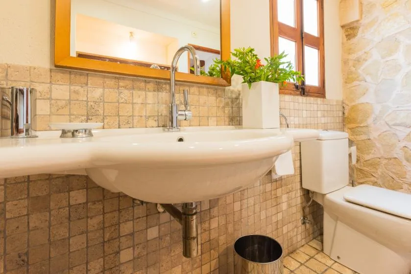 A tiled bathroom with a wide sink, toilet, and window.