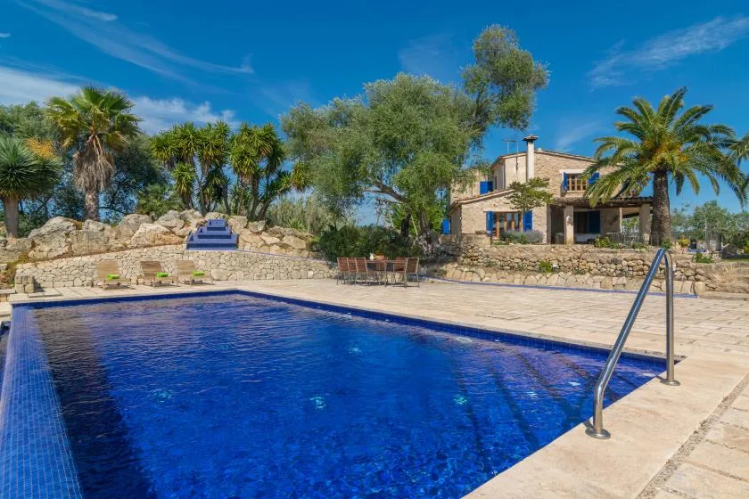 An outdoor swimming pool sits beside a stone house and landscaped garden.
