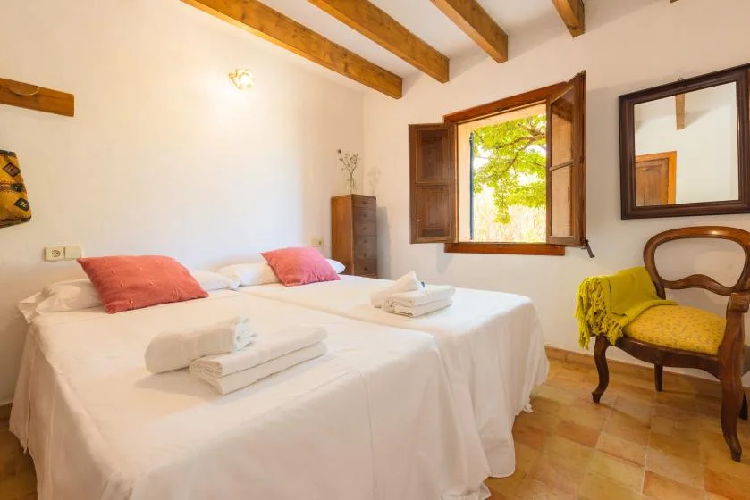 A bedroom with two beds, folded towels, and a window overlooking greenery.