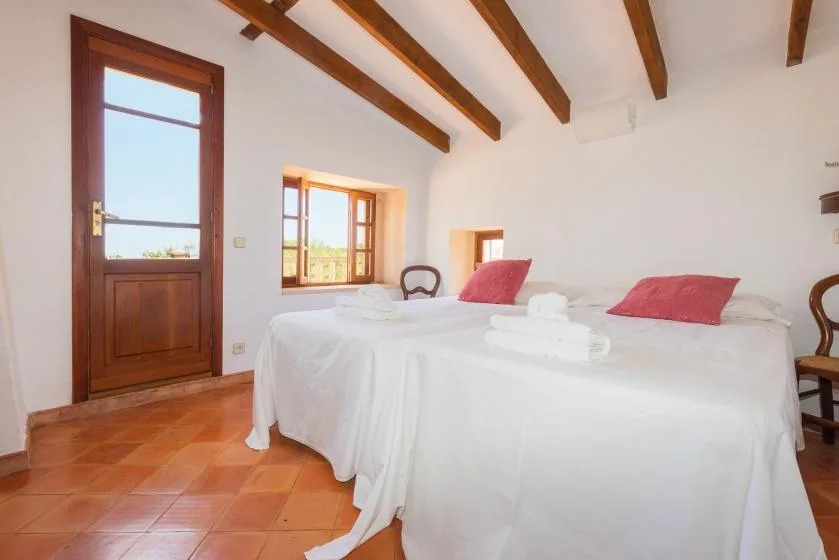 A bright bedroom with white bedding and exposed wooden ceiling beams.
