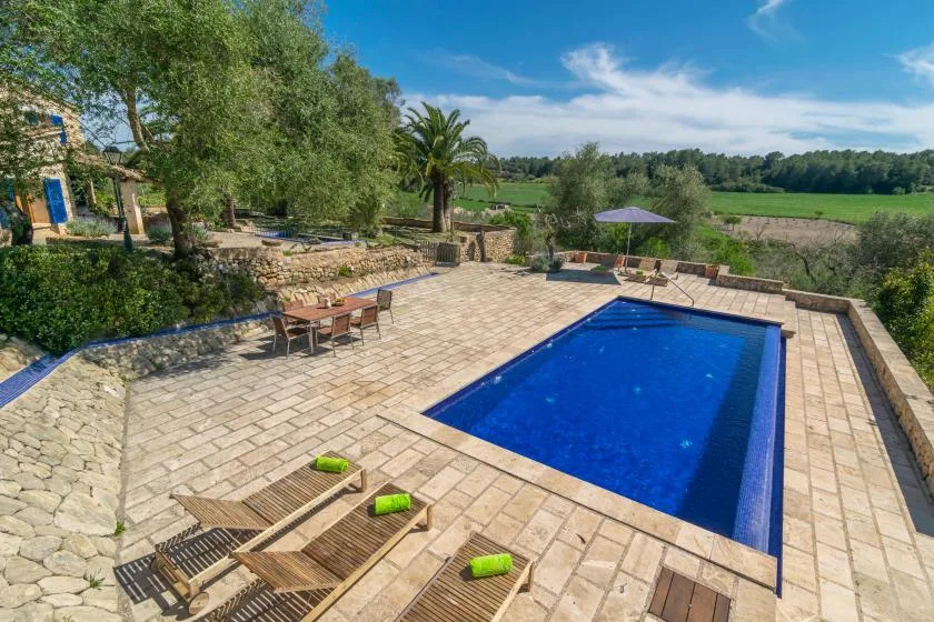 A blue swimming pool sits within a spacious stone-paved outdoor terrace.