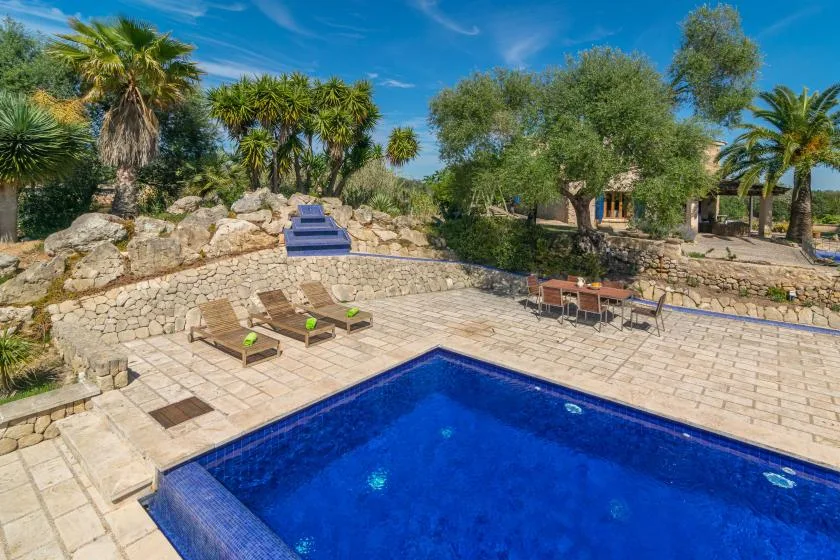 An outdoor swimming pool sits beside a paved terrace and landscaped garden.