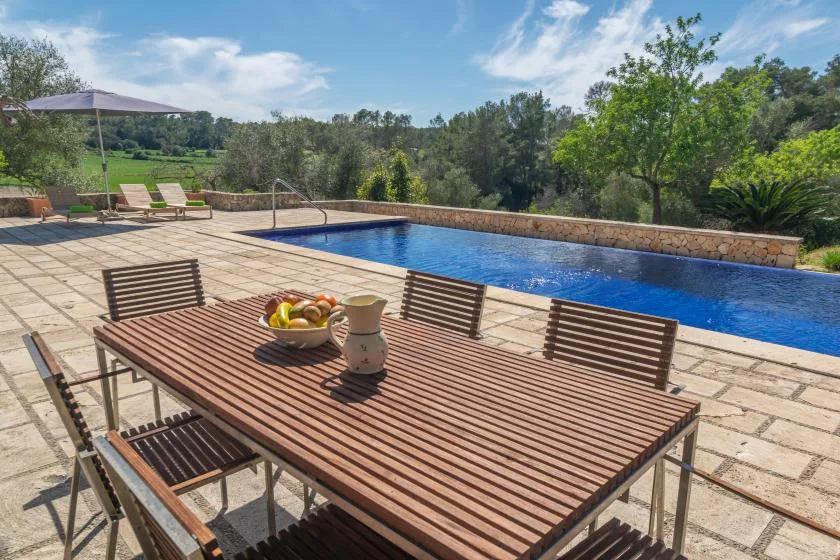 A tiled outdoor patio with a dining table beside a swimming pool.