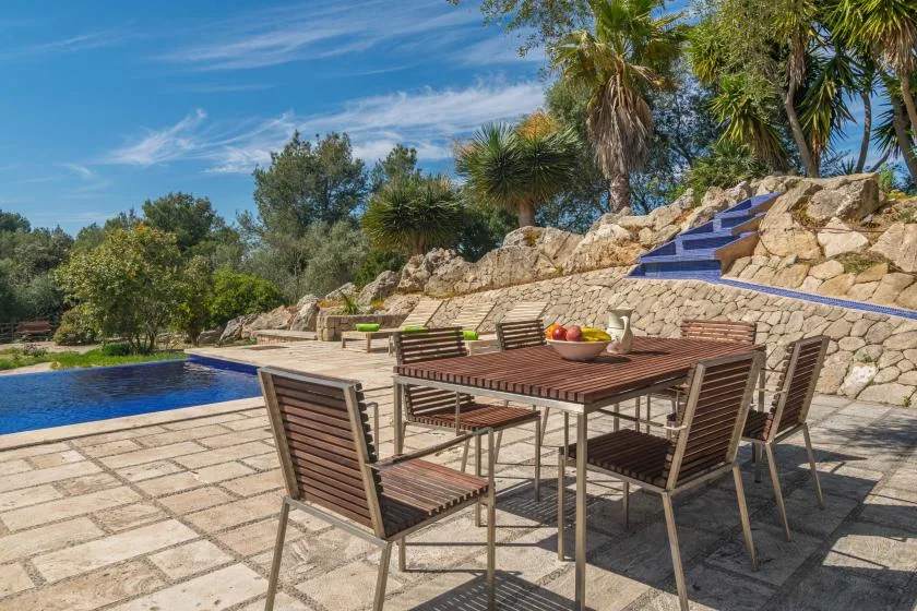 A patio dining area beside a swimming pool, with a stone wall and steps.