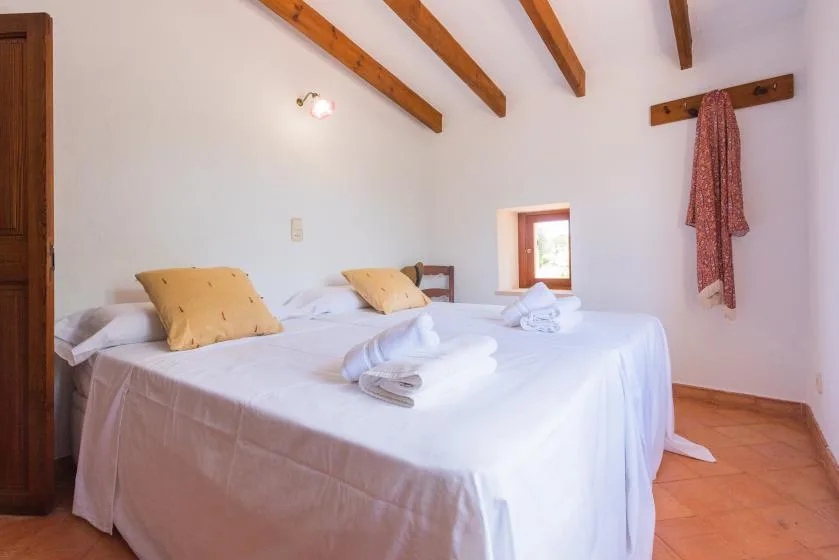 A bedroom with two beds, white linens, and exposed wooden ceiling beams.