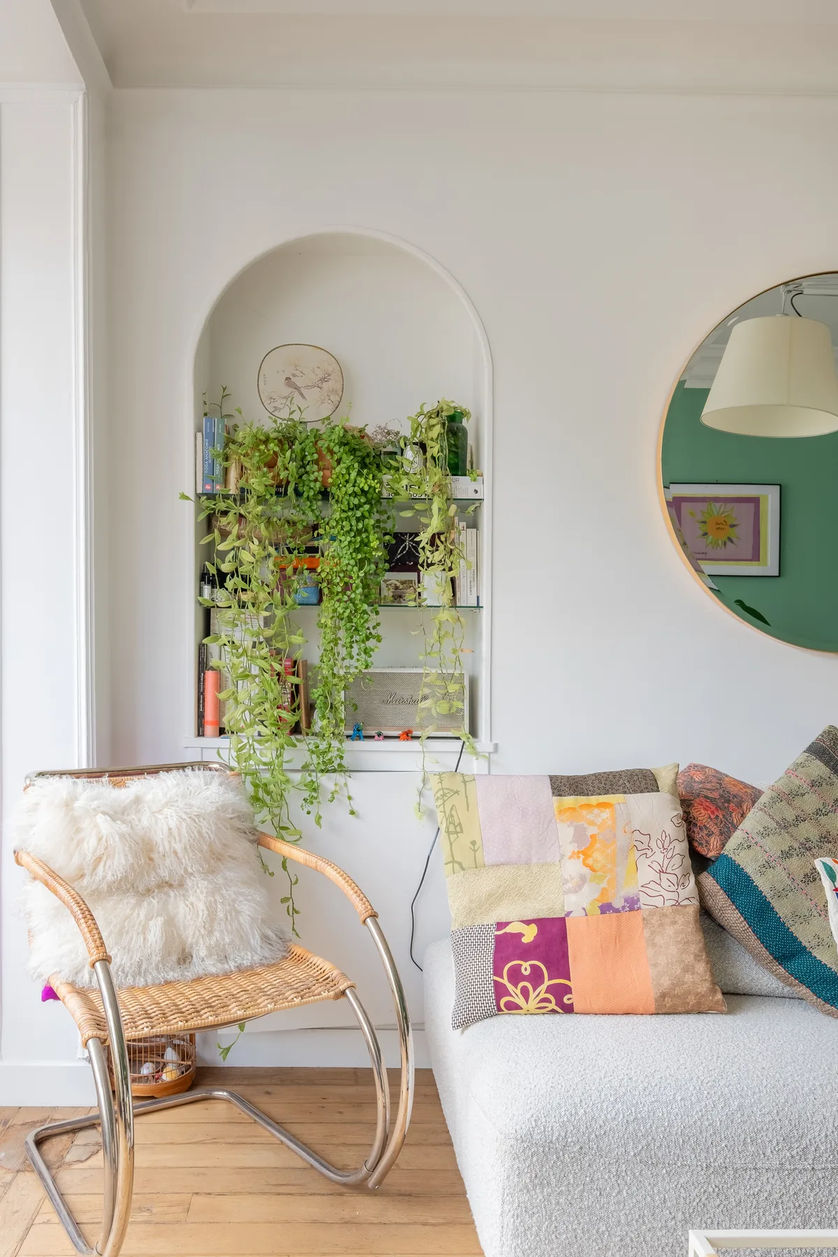 Una sala luminosa con un asiento acolchado, una silla tejida y plantas en un estante.