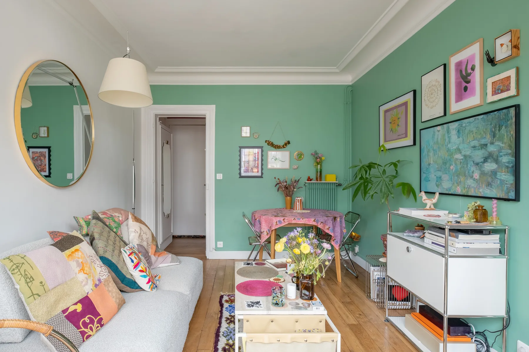 A colorful living room with a sofa, framed artwork, and a small dining table.