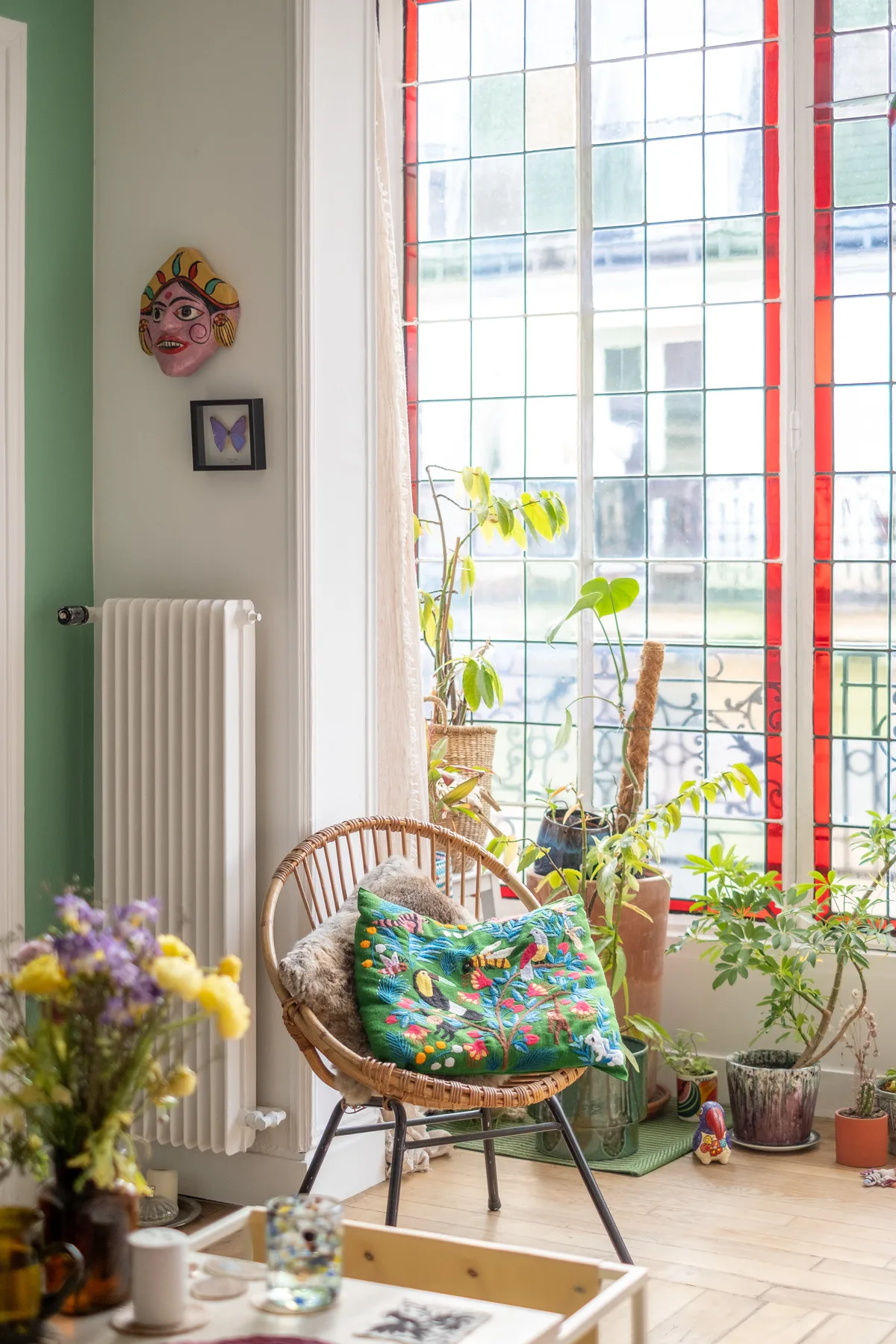 Una luminosa zona de estar con una silla tejida, un cojín colorido y plantas junto a una ventana grande.