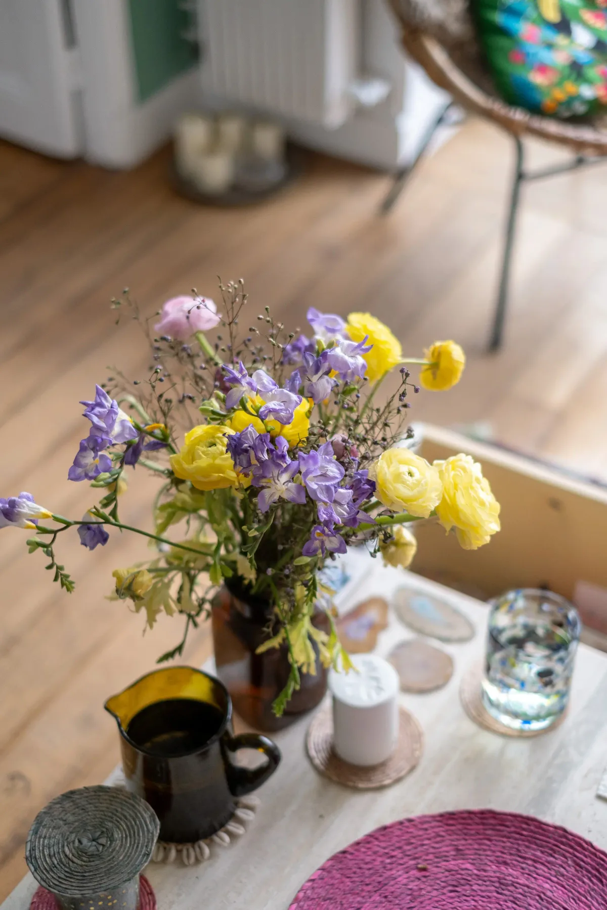 Un arreglo de flores está sobre una mesa junto a un vaso y una taza de cerámica.
