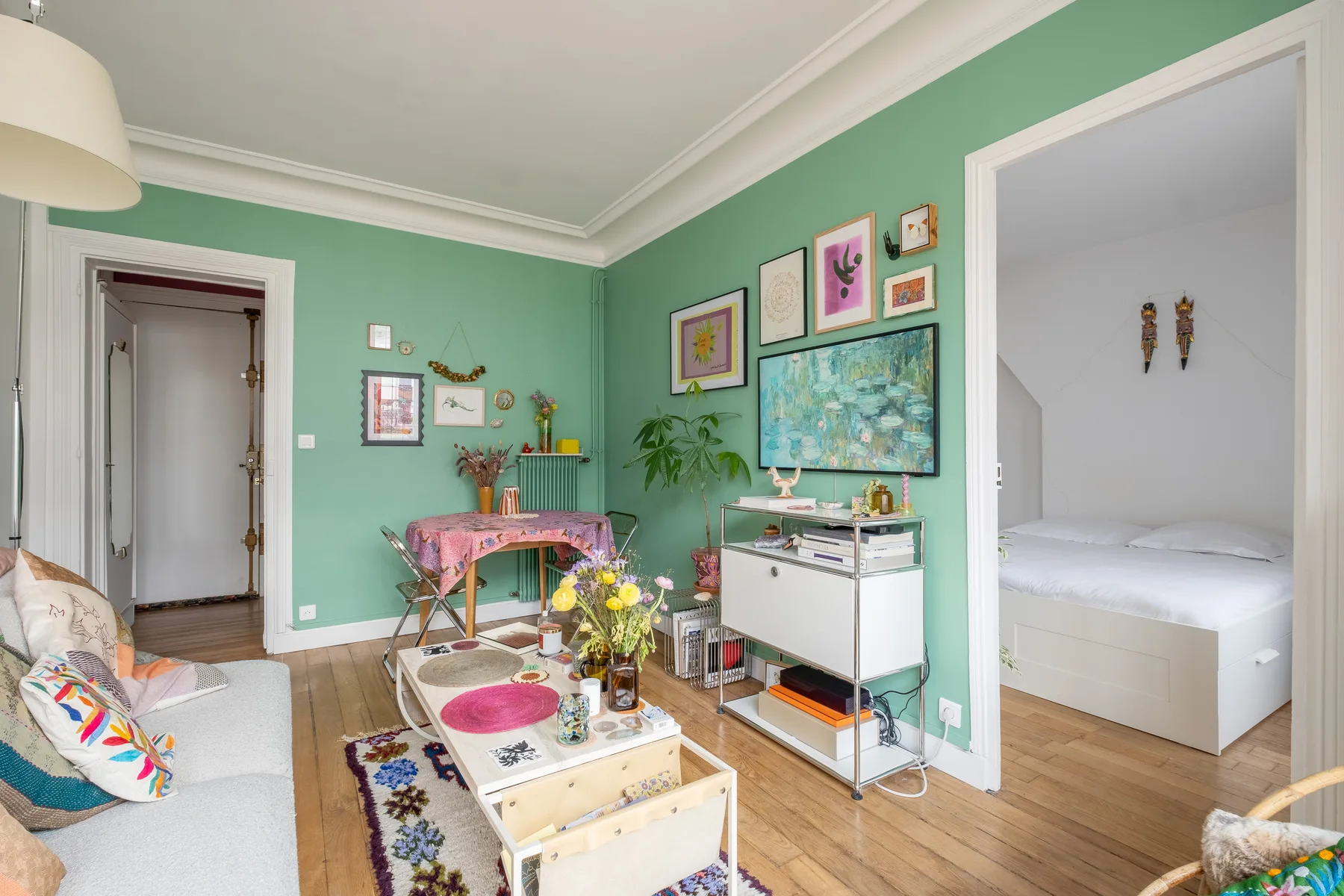 A green living room with seating, colorful artwork, and an open doorway to a bedroom.