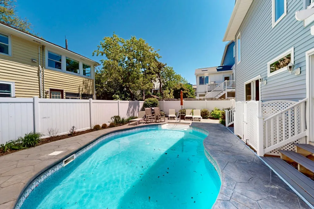 An outdoor swimming pool beside a house, with patio seating along the edge.