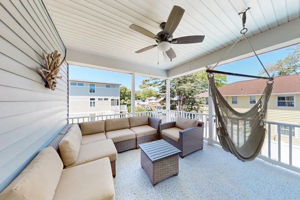 A covered outdoor seating area with cushioned furniture, a ceiling fan, and a hanging chair.