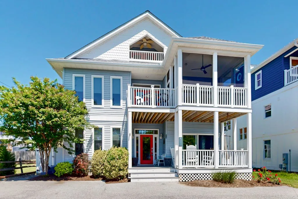 A light-colored house with two covered porches and a red front door.