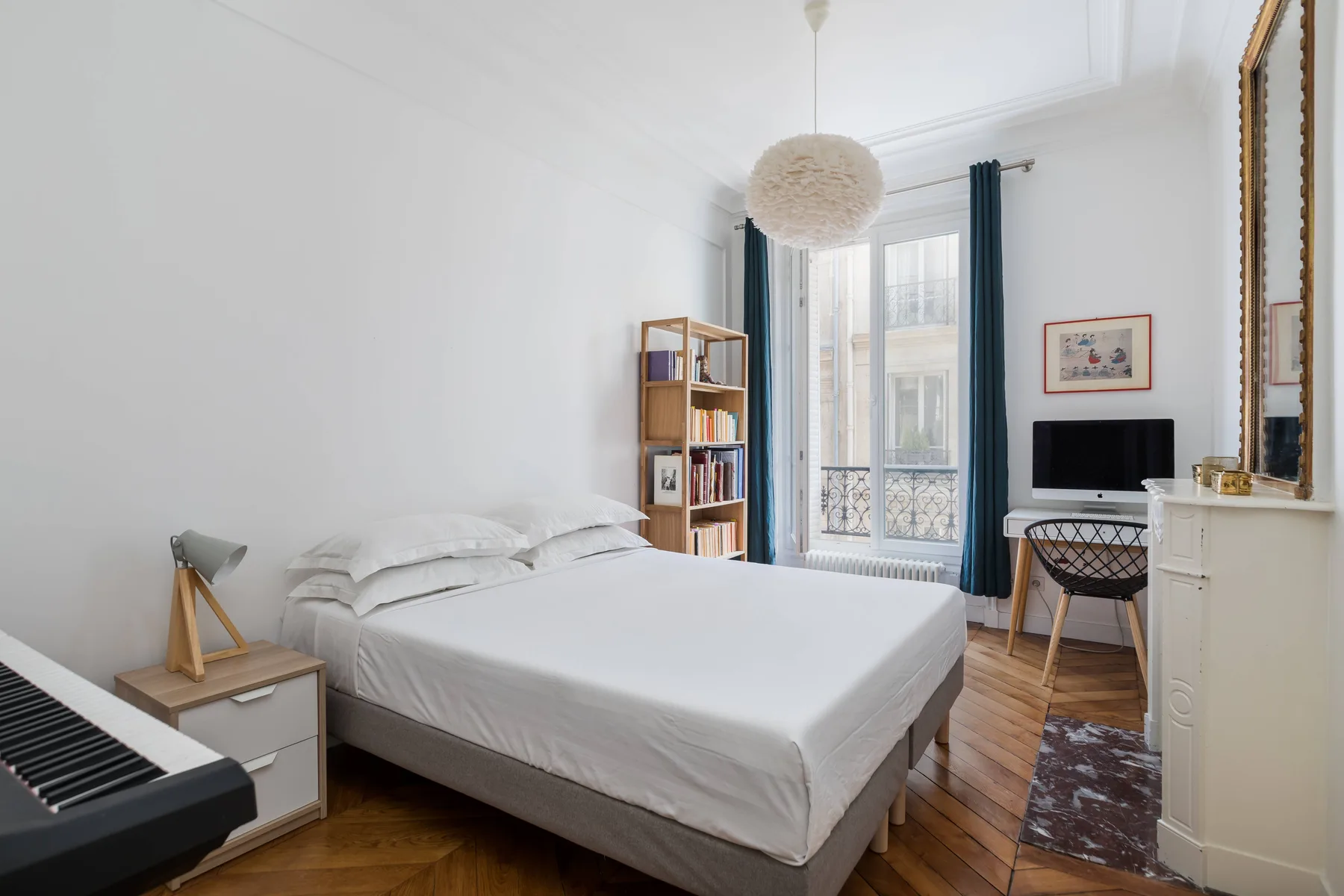 A bright bedroom with a neatly made bed and a tall window with dark curtains.