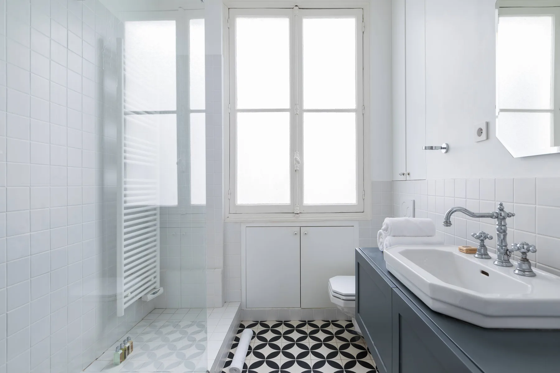 A bright tiled bathroom with a bathtub beneath the window.