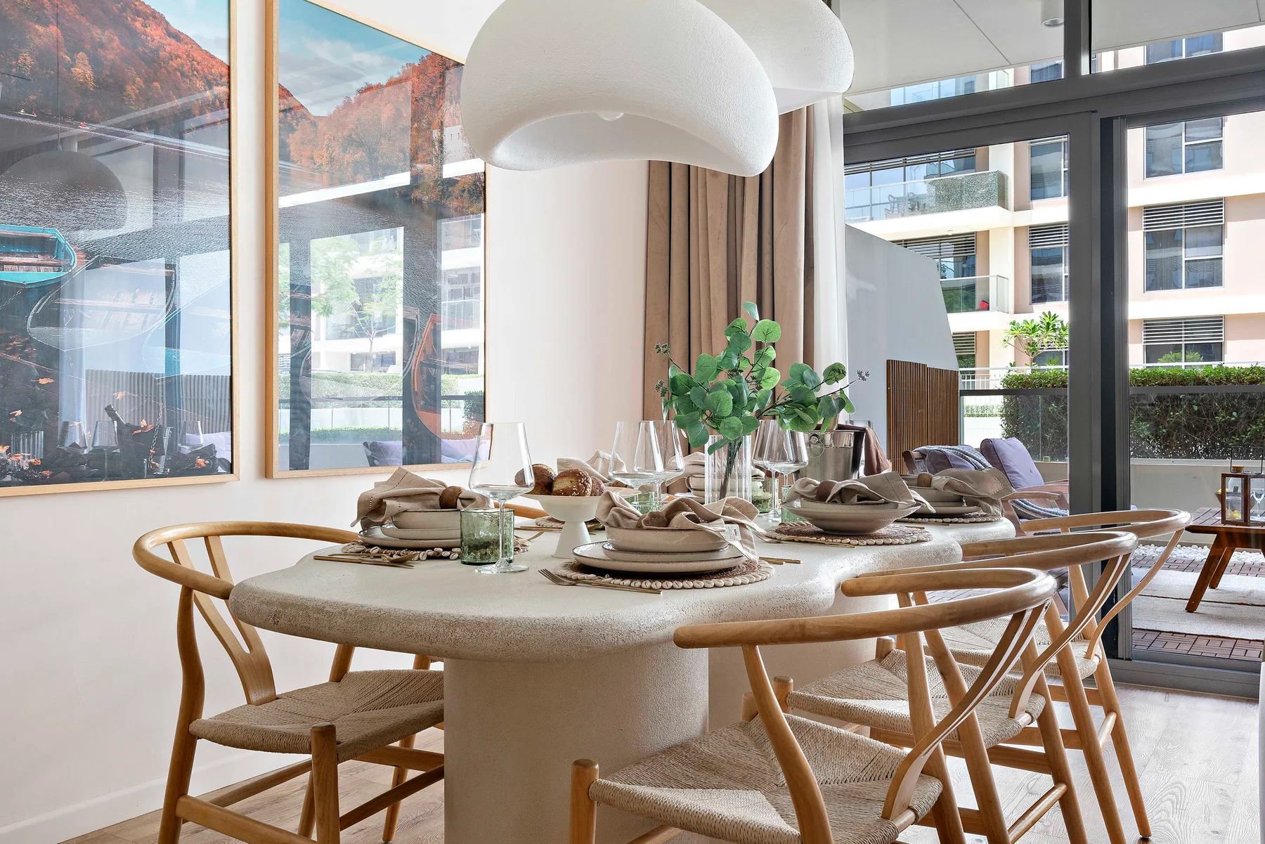 Un comedor con la mesa puesta, asientos de madera y ventanales.