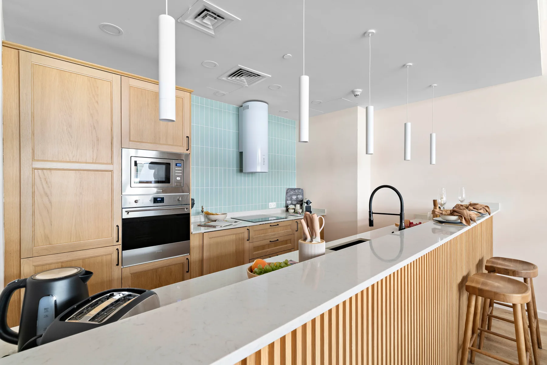 Una cocina luminosa con una isla larga, gabinetes de madera y lámparas colgantes.