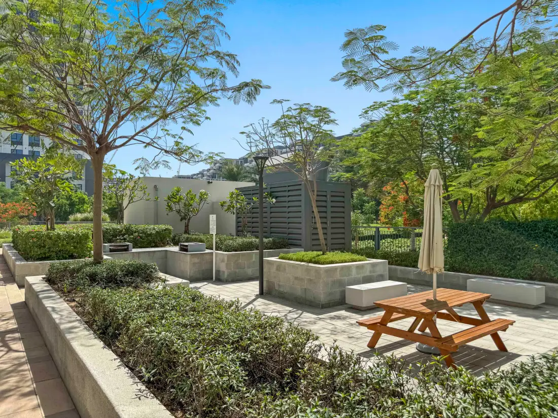 Un patio exterior ajardinado con jardineras elevadas, árboles y mesas de picnic.