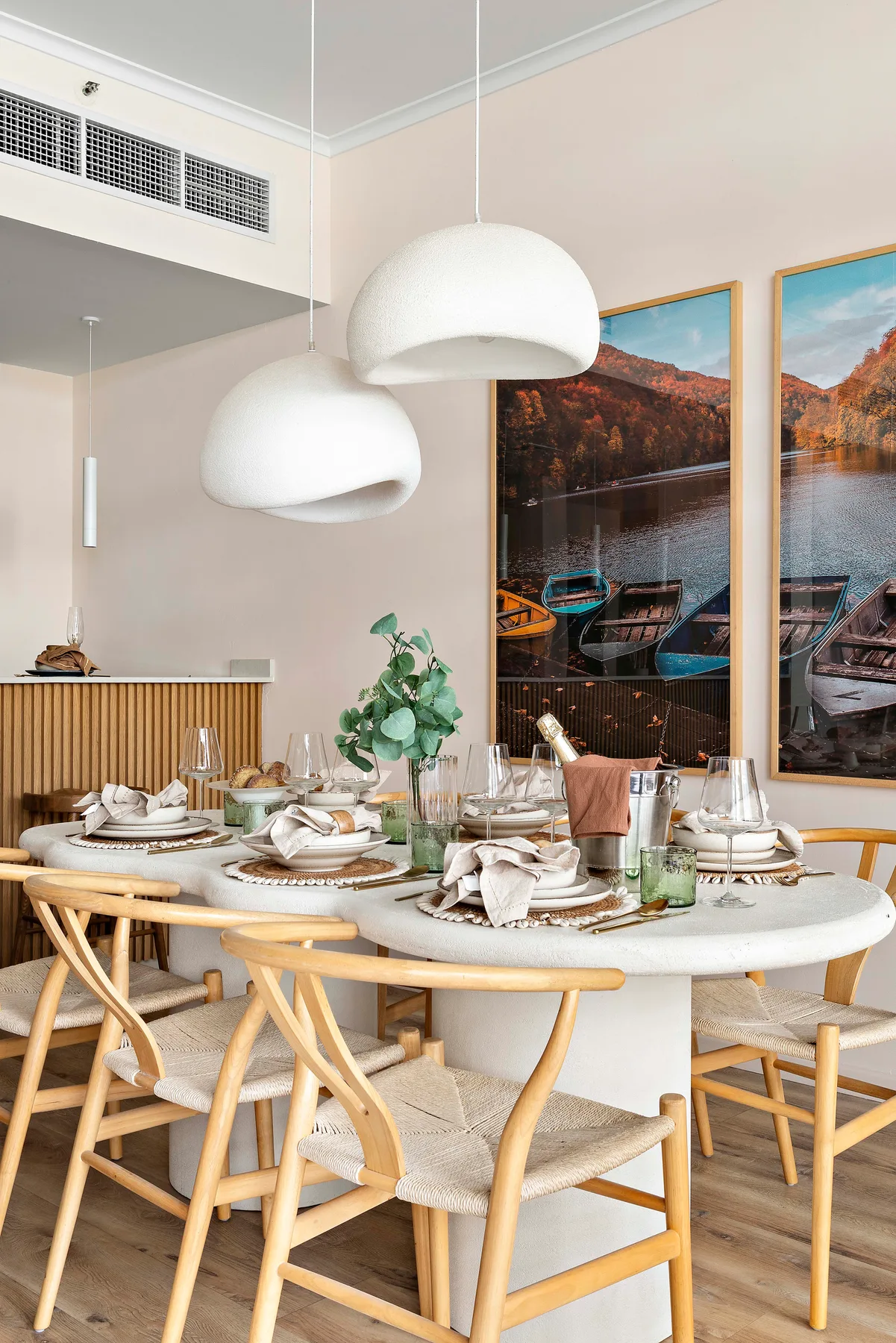 Comedor con la mesa puesta, asientos tejidos y lámparas colgantes.