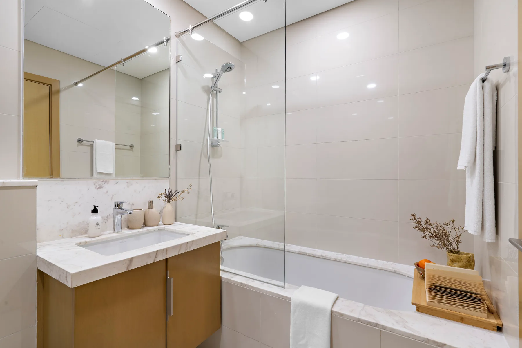 Un baño luminoso con lavabo, espejo y bañera con ducha.