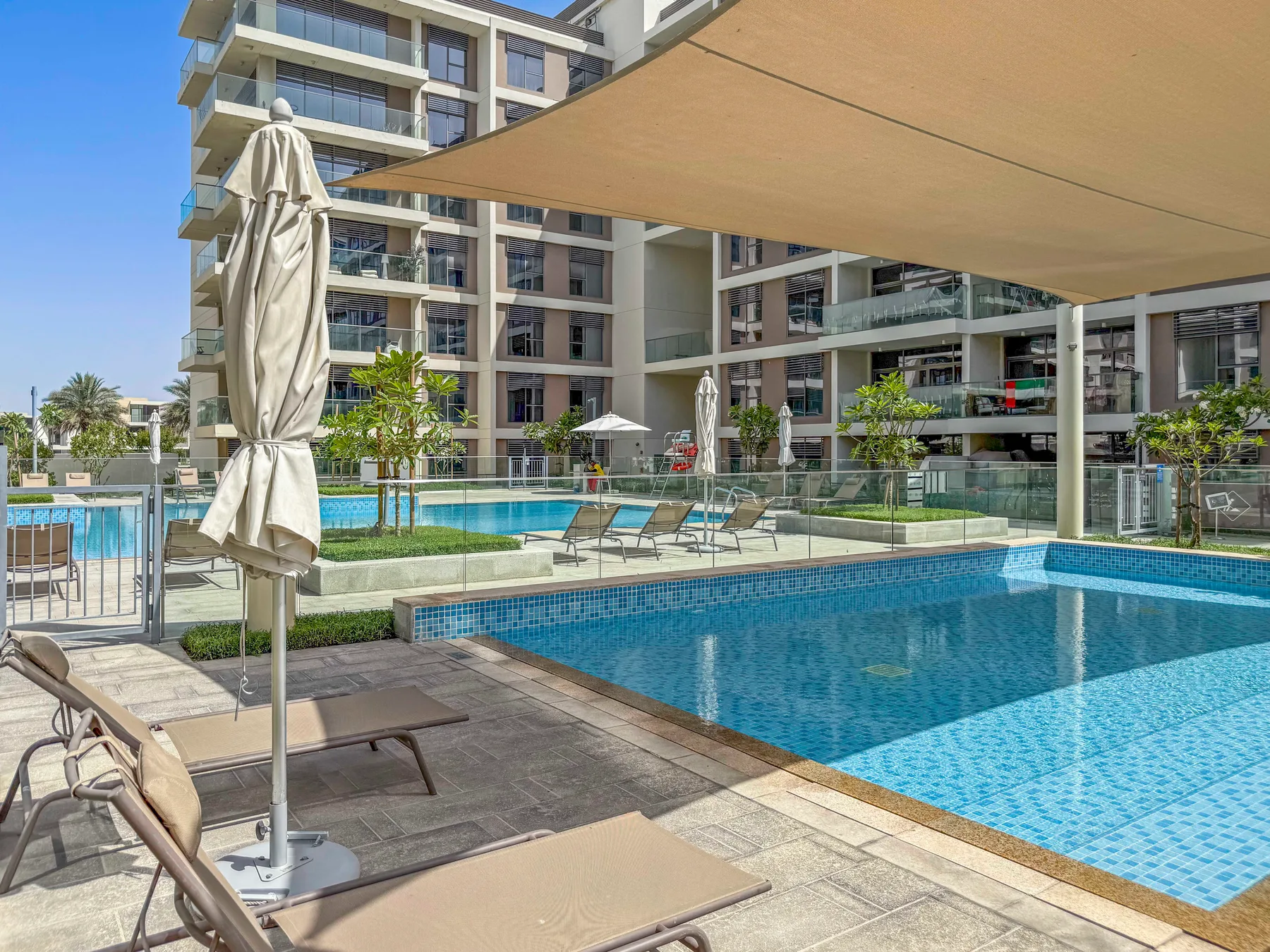 Una piscina al aire libre junto a un edificio moderno, con asientos y sombra.