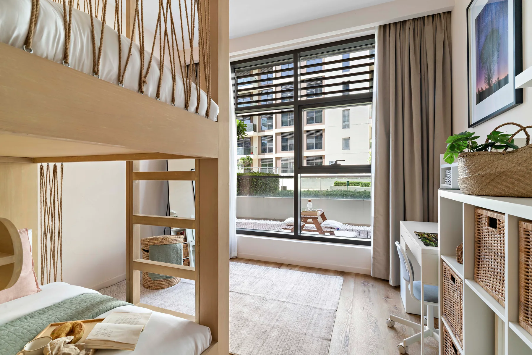 Dormitorio luminoso con cama alta, grandes ventanas y una alfombra clara.