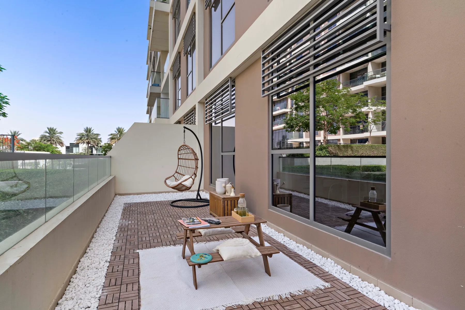 Un patio exterior pavimentado con una silla colgante y una mesa baja junto a grandes ventanales.