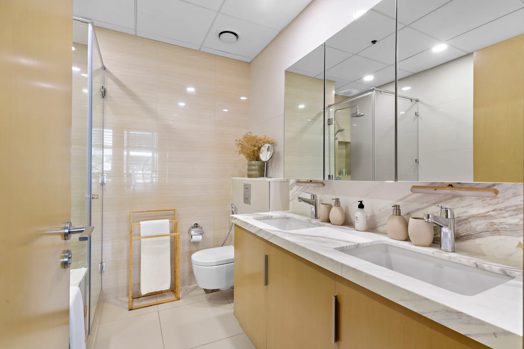 Un baño luminoso con un tocador largo, espejos y una ducha de vidrio.
