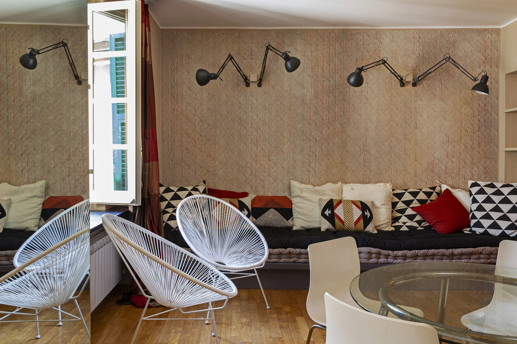 A living room with patterned seating and white woven chairs around a glass table.