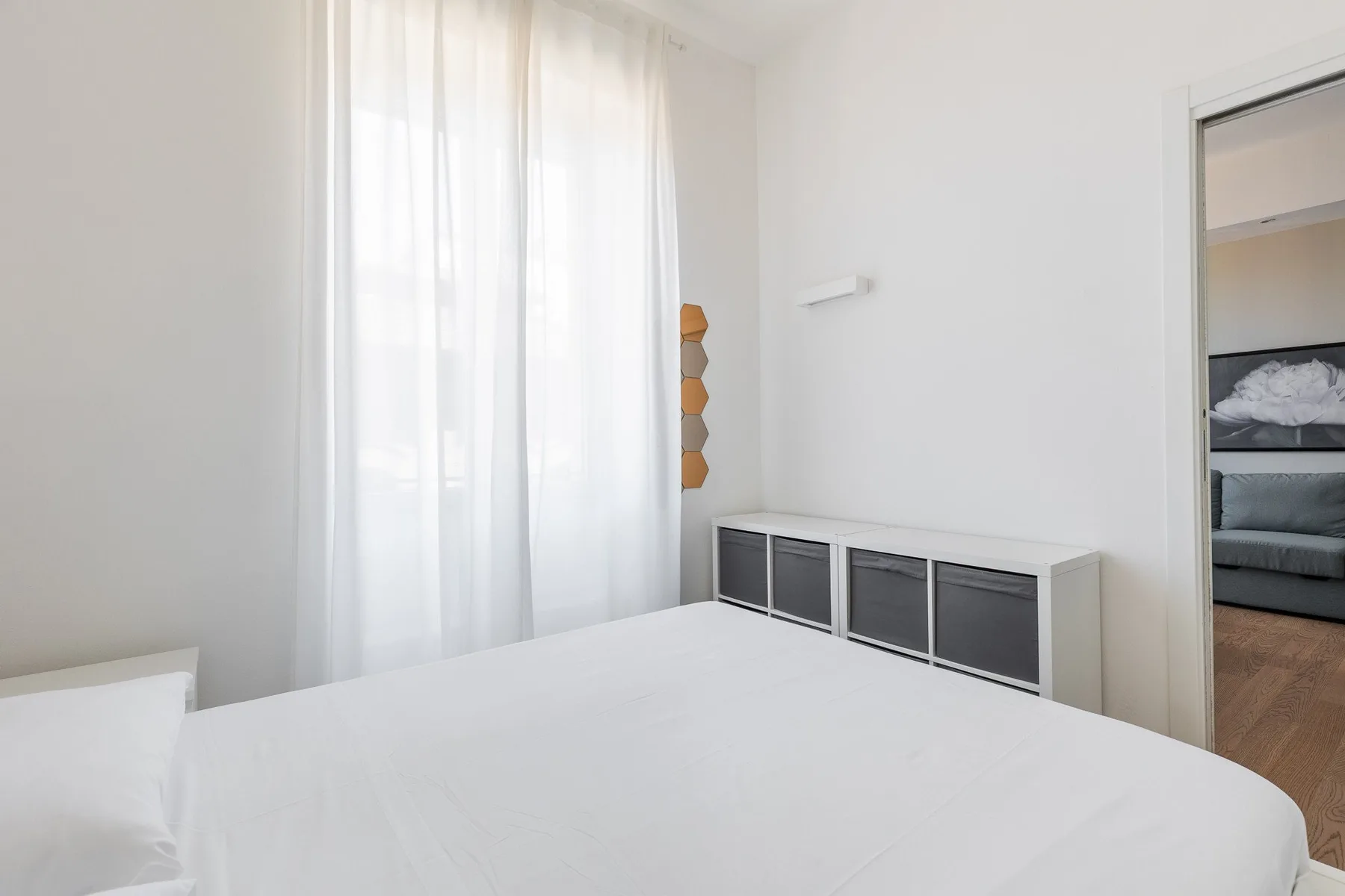 Un dormitorio luminoso con una cama blanca junto a una ventana con cortinas.
