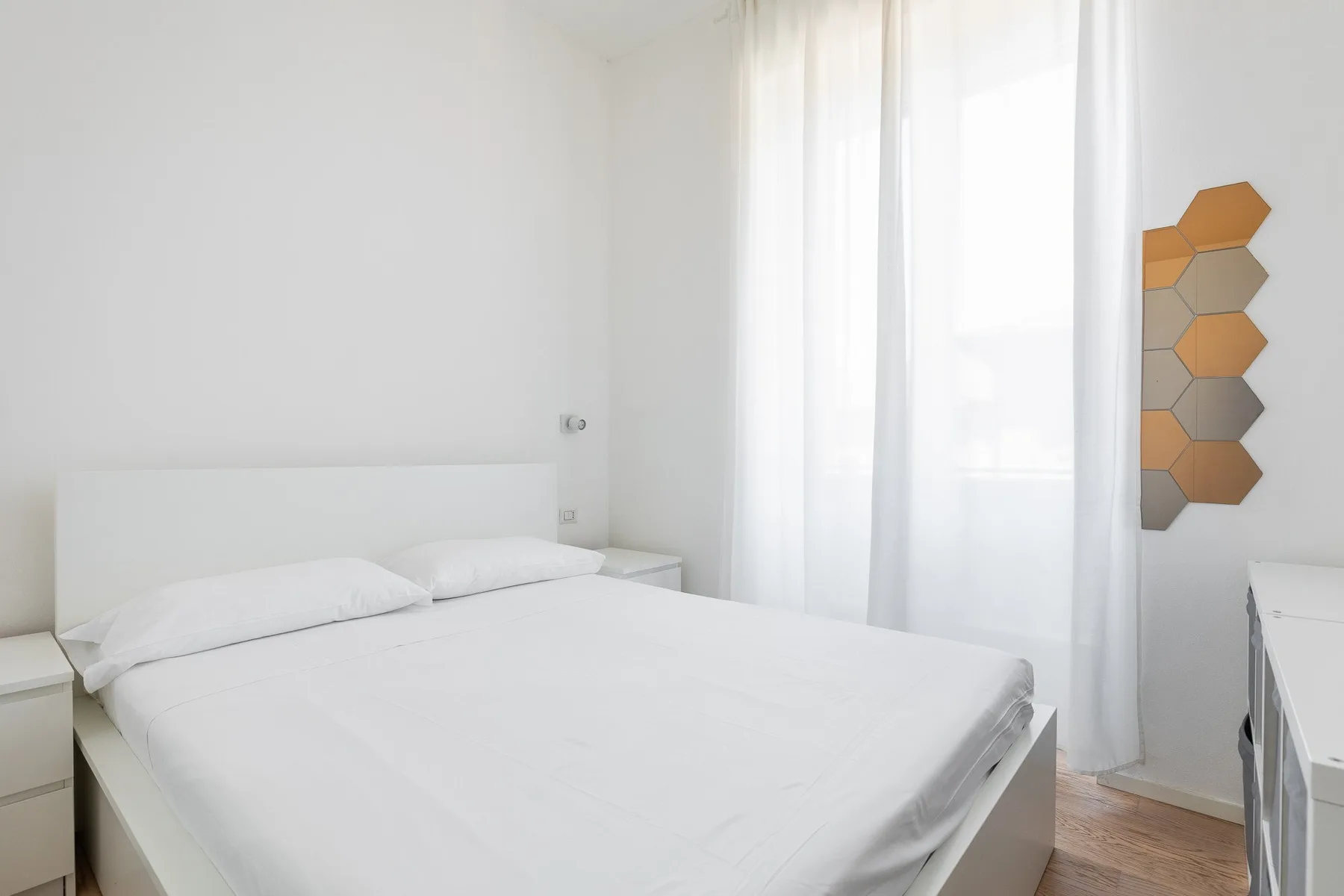 Un dormitorio luminoso con una cama grande junto a cortinas translúcidas.