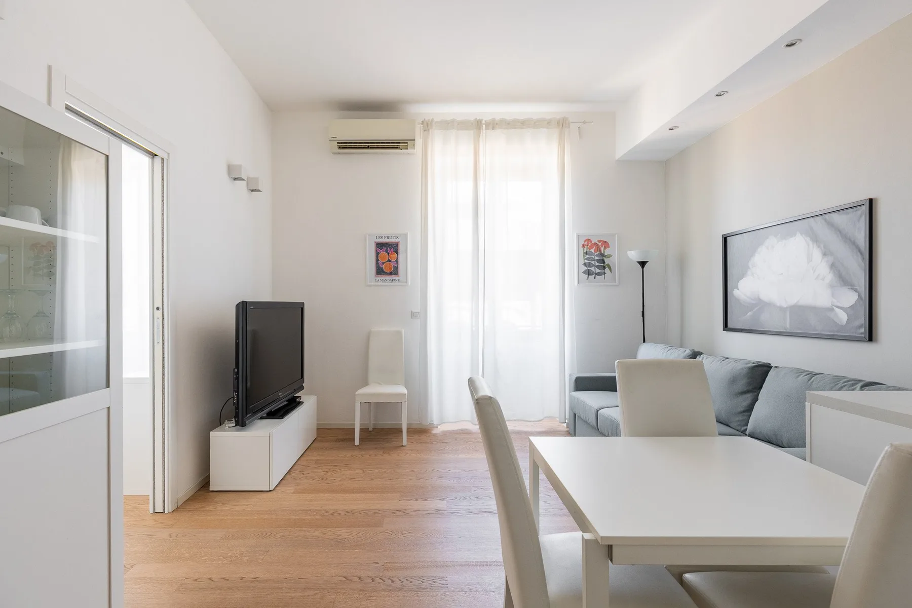 Una luminosa sala de estar y comedor con televisor, asientos y una mesa junto a la ventana.