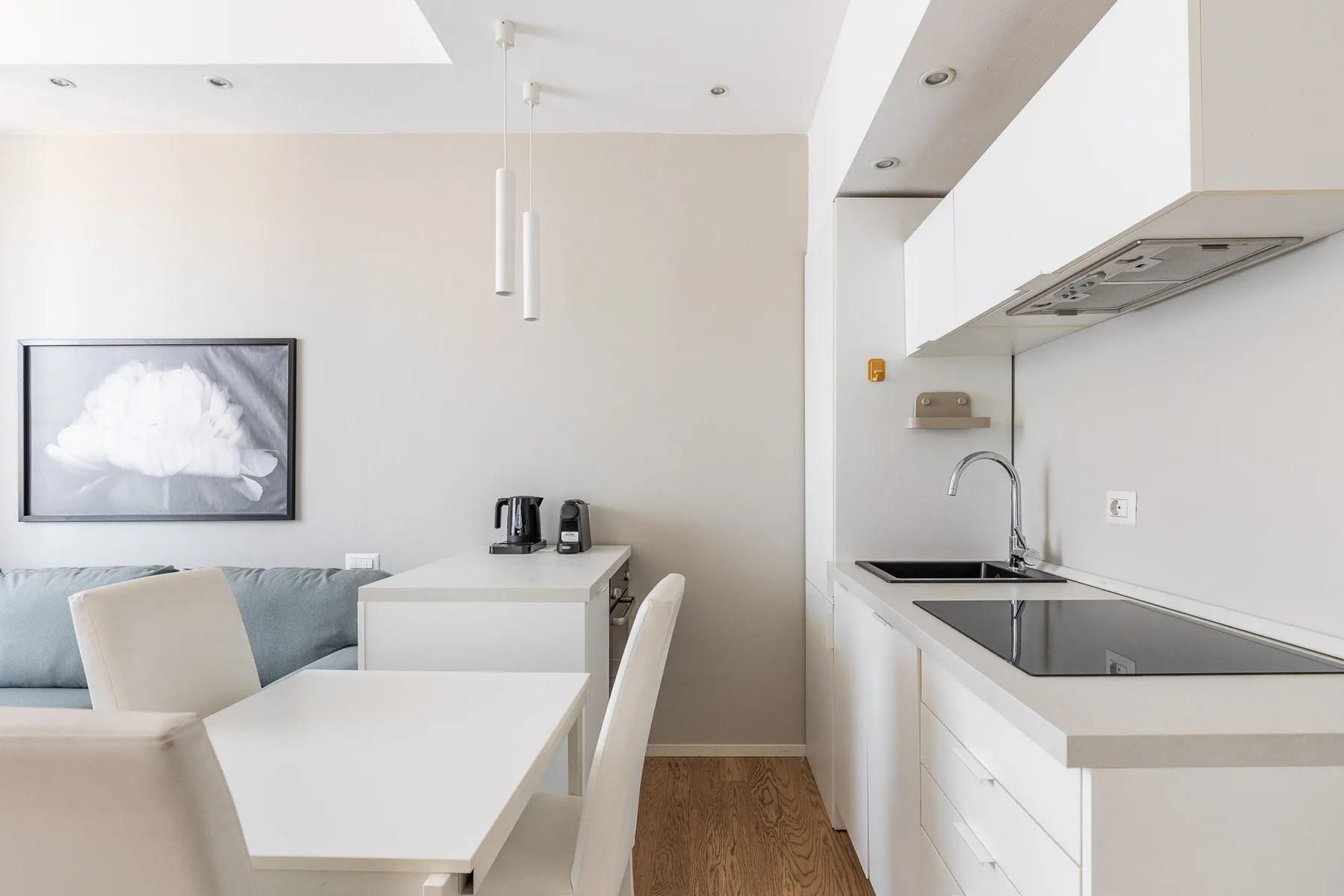Un comedor luminoso junto a una cocina compacta con gabinetes y encimeras blancos.