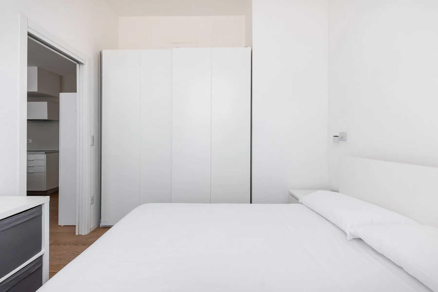 Un dormitorio luminoso con una cama blanca y un armario alto.