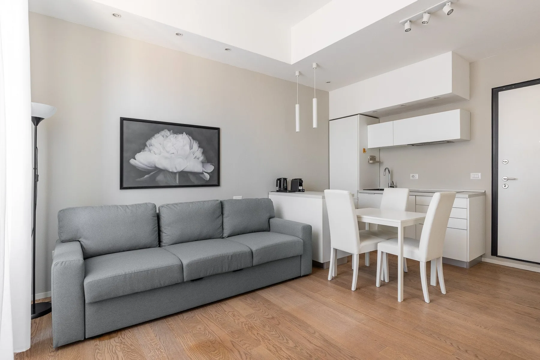 Una luminosa sala de estar y comedor con asientos grises, una mesa y una cocina compacta.