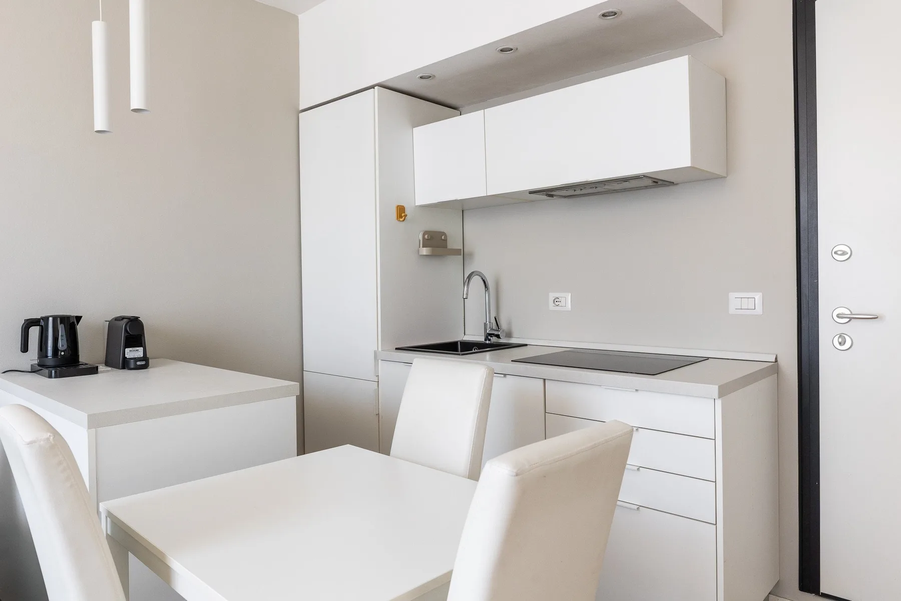 Una cocina compacta con zona de comedor, armarios blancos y una mesa.