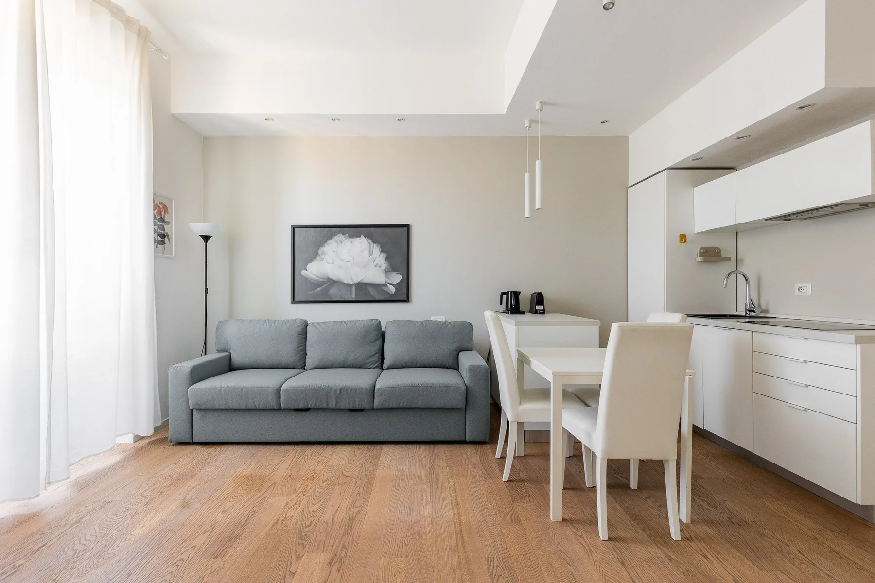 Una luminosa sala-comedor de planta abierta con un sofá gris junto a una cocina blanca.