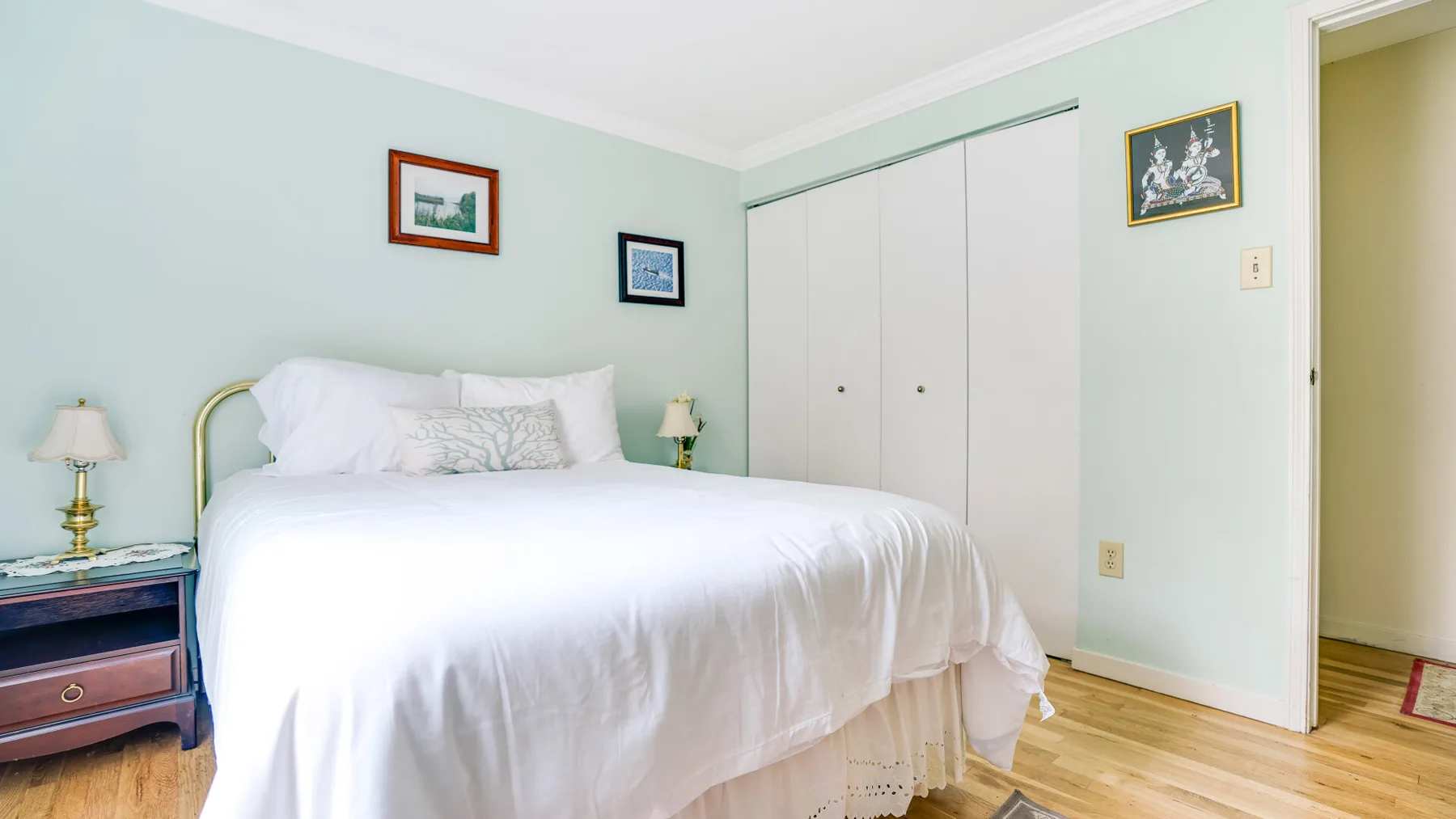 A bedroom with a white bed, pale green walls, and light wood flooring.