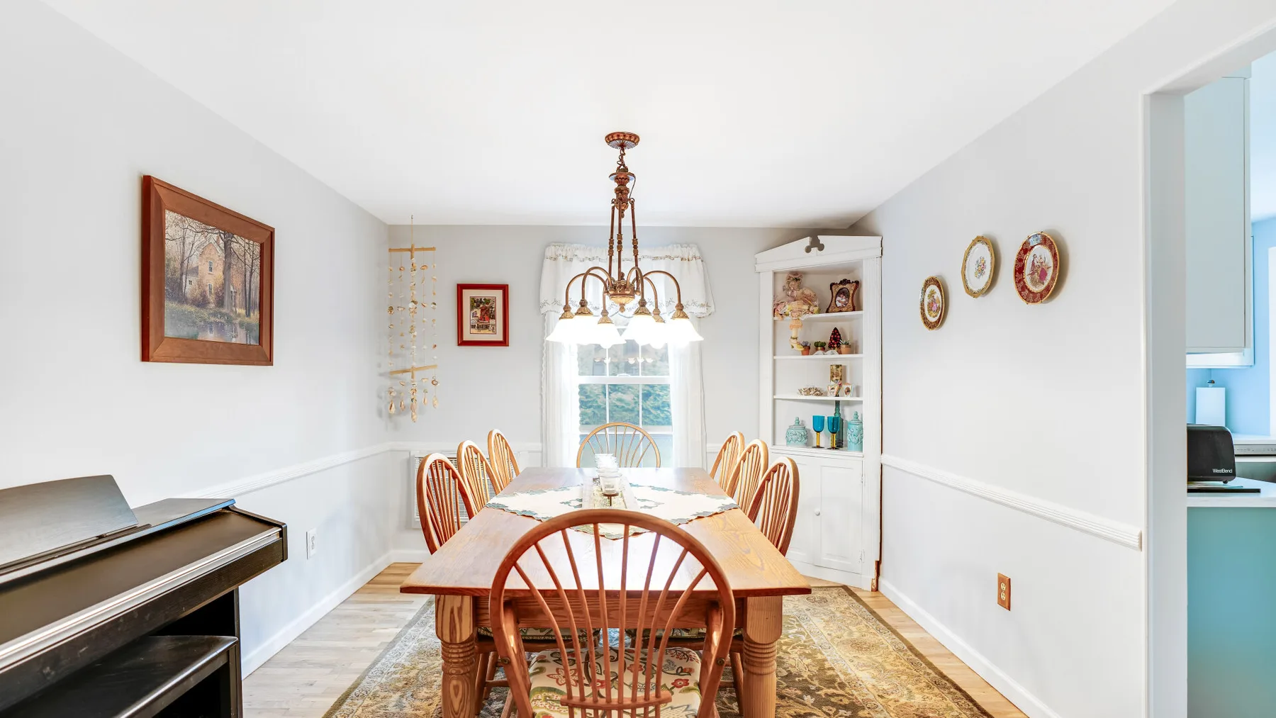 A bright dining room with a wooden table, chairs, and a piano.