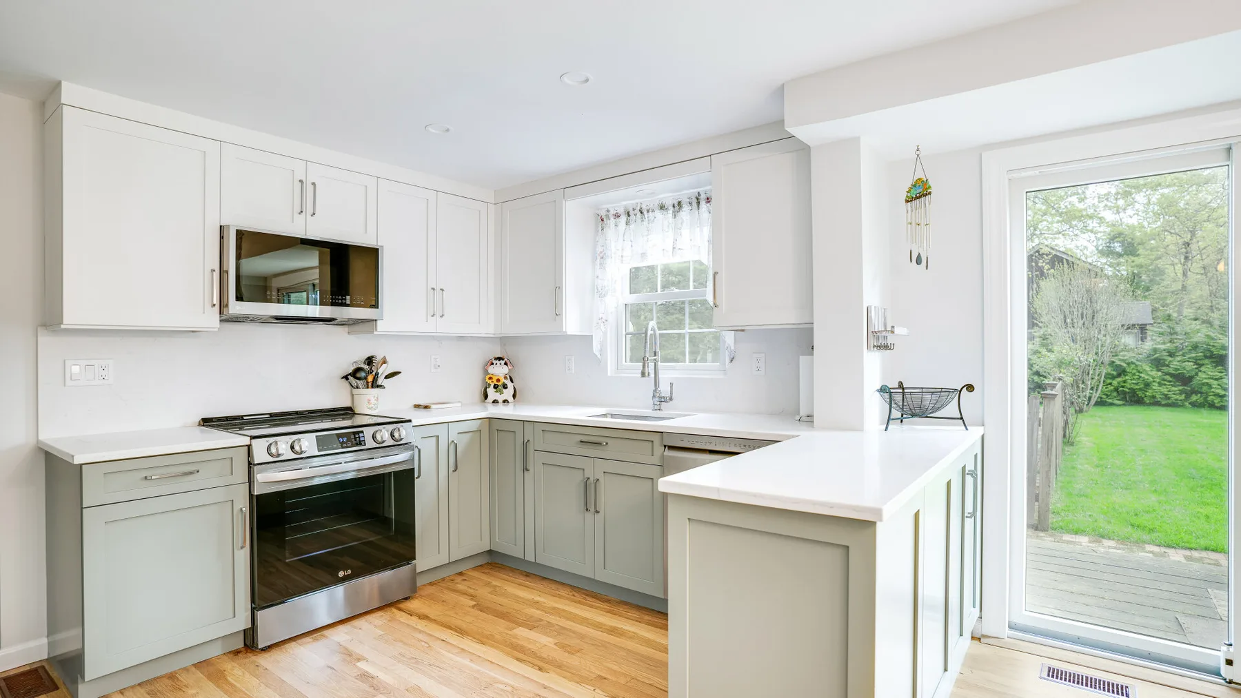 A bright kitchen with white cabinetry, a stove, and a glass door to the garden.
