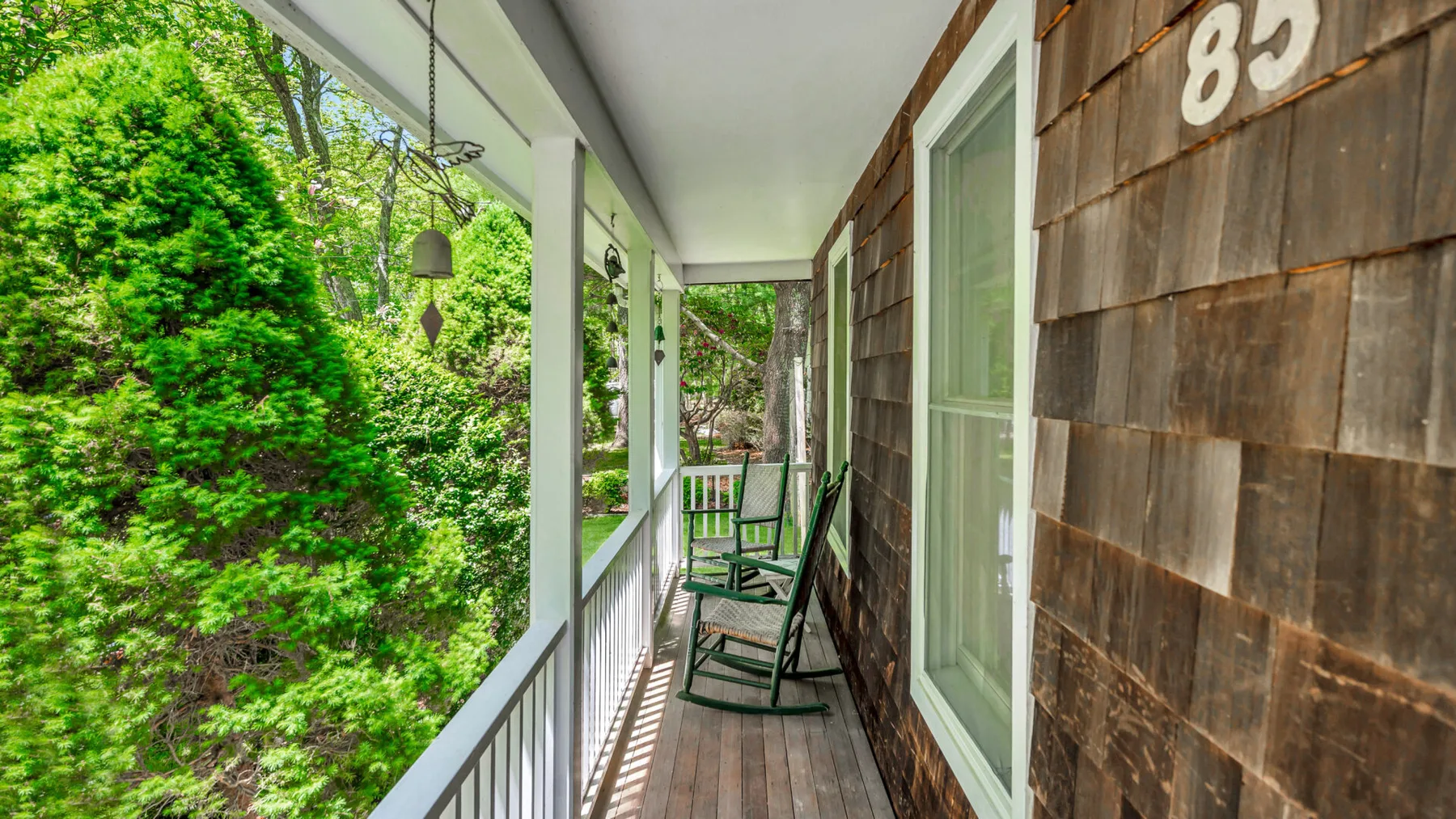 A covered porch with green rocking chairs and views of leafy trees.
