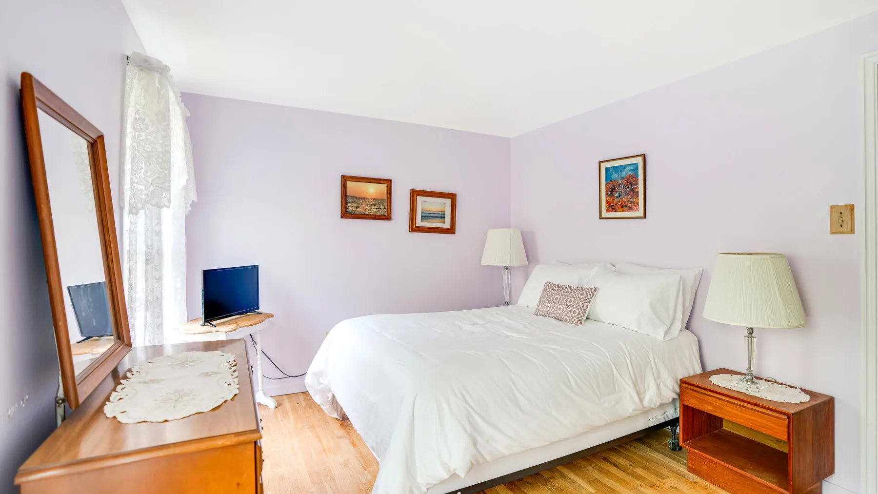 A bedroom with a neatly made bed, bedside tables, and framed pictures on the walls.