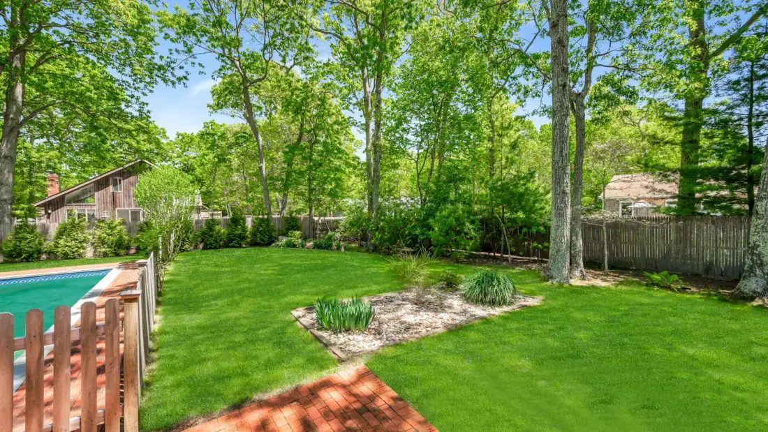 A tree-lined backyard with a lawn, garden beds, and a swimming pool.