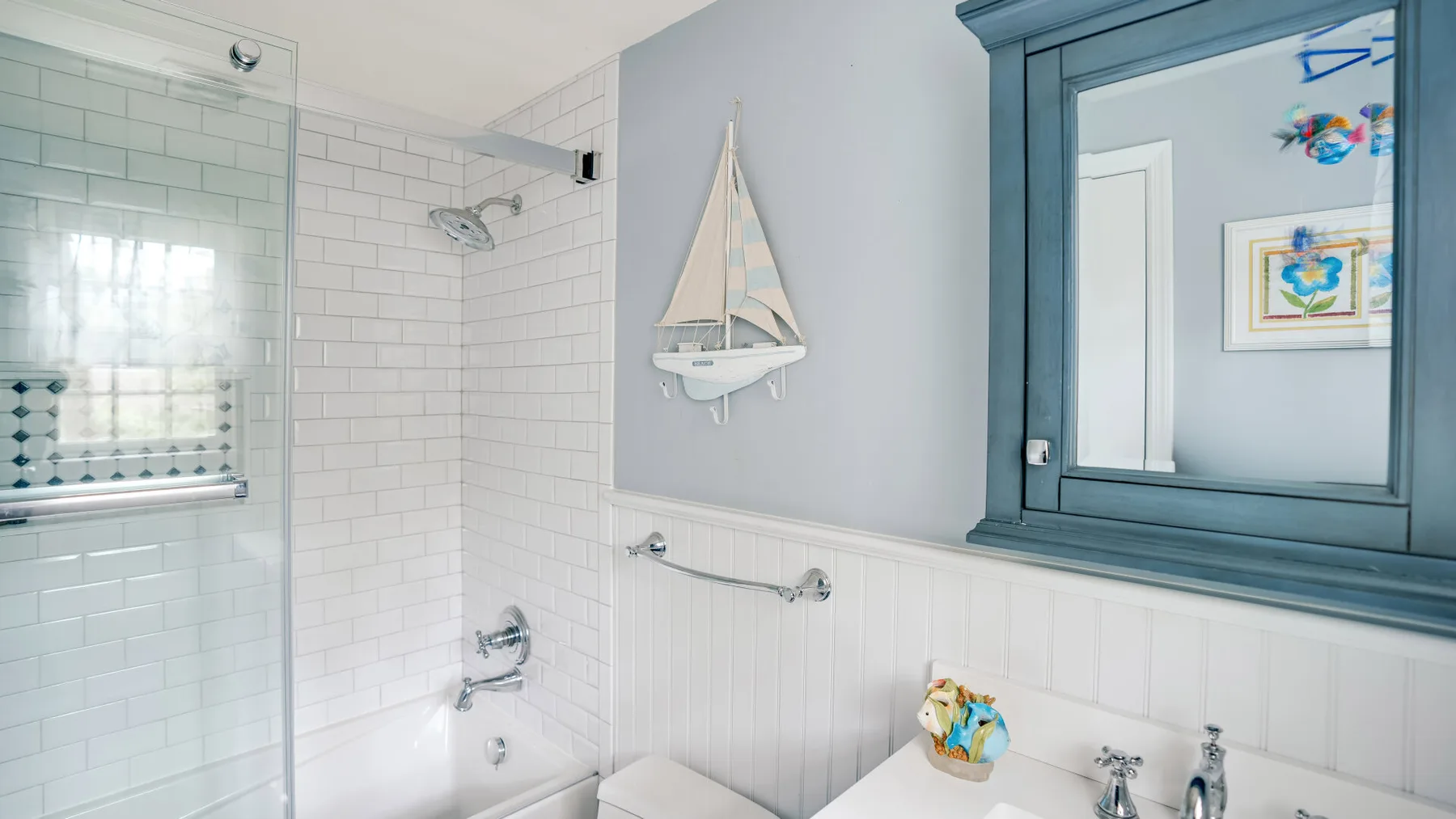 A tiled bathroom with a glass shower and a framed mirror above the sink.