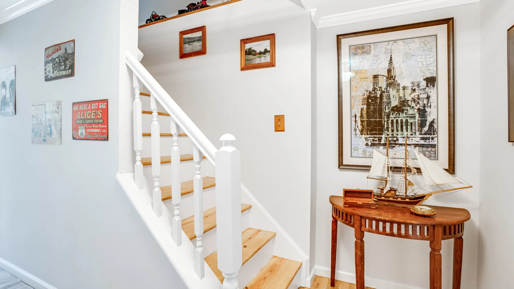 A staircase with framed wall art and a wooden table holding a model ship.